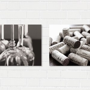 May include: Black and white photograph featuring two distinct compositions. One side showcases a close-up of wine glasses, while the other presents a collection of wine corks, some with visible text. The image is set against a white brick wall.