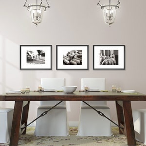 May include: A dining room with a wooden table and white chairs. Three black framed photos hang on the wall above the table. The photos are black and white and feature a variety of subjects.