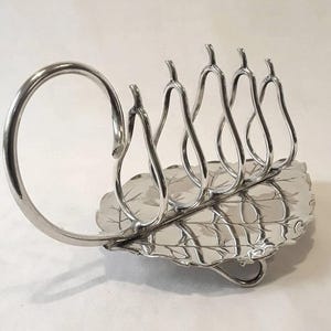 Può includere: Porta toast argentato con base a forma di foglia e divisori a forma di pera. Il porta toast ha un manico curvo ed è progettato per contenere più fette di pane tostato. La base a forma di foglia aggiunge un tocco decorativo.