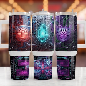 May include: A stainless steel tumbler with a handle featuring a Transformers theme. The design displays a red Autobot logo, a glowing blue Energon crystal, and a purple Decepticon logo over a dark mechanical circuit board pattern with digital HUD graphics.