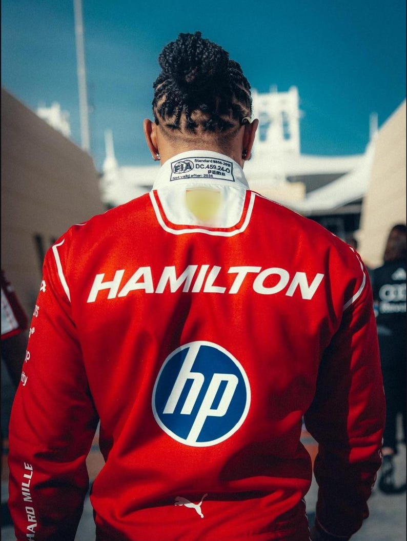 Pode incluir: Casaco de corrida vermelho com detalhes brancos e o nome "HAMILTON" em letras brancas grandes. O logotipo da HP est&aacute; no casaco, juntamente com o logotipo da Puma. O casaco tem uma gola branca com a marca FIA e Puma.