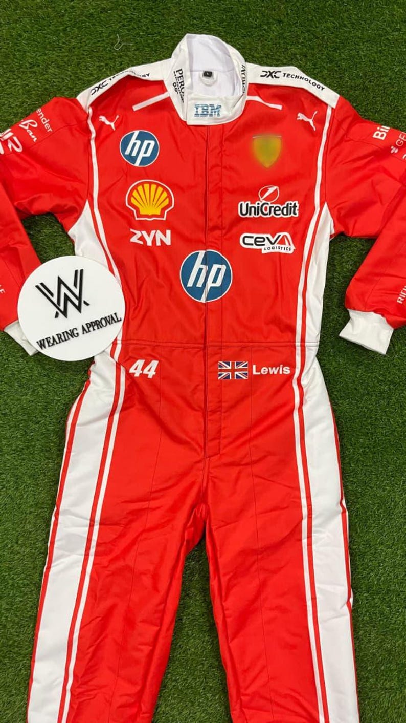 Pode incluir: Macac&atilde;o de corrida vermelho e branco com logotipos de patrocinadores, incluindo HP, Shell e IBM. O macac&atilde;o apresenta o n&uacute;mero 44, o nome "Lewis" e uma bandeira brit&acirc;nica. Listras brancas nas laterais. Em uma superf&iacute;cie verde.
