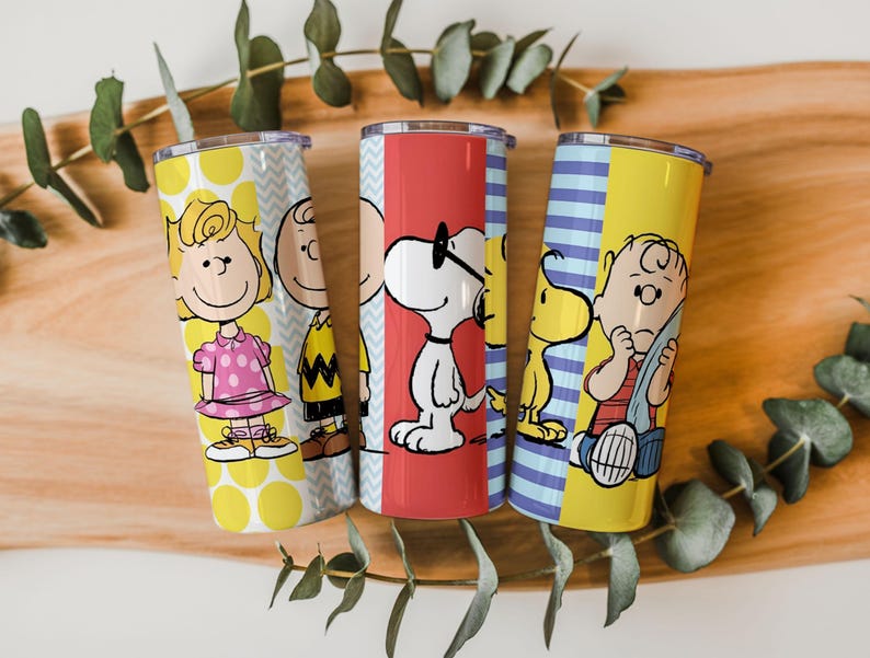 Puede incluir: Tres vasos de acero inoxidable con personajes de Peanuts. Un vaso tiene a Sally Brown, otro a Charlie Brown y el tercero a Snoopy. Los vasos tienen bloques de color amarillo, rojo y azul con fondos estampados.