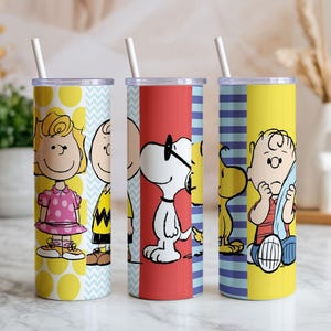 Puede incluir: Tres vasos de acero inoxidable con pajitas blancas, con personajes de Peanuts. Un vaso tiene a Sally Brown, otro a Snoopy y el tercero a Charlie Brown. Los vasos tienen fondos amarillos, rojos y azules con dise&ntilde;os de personajes.