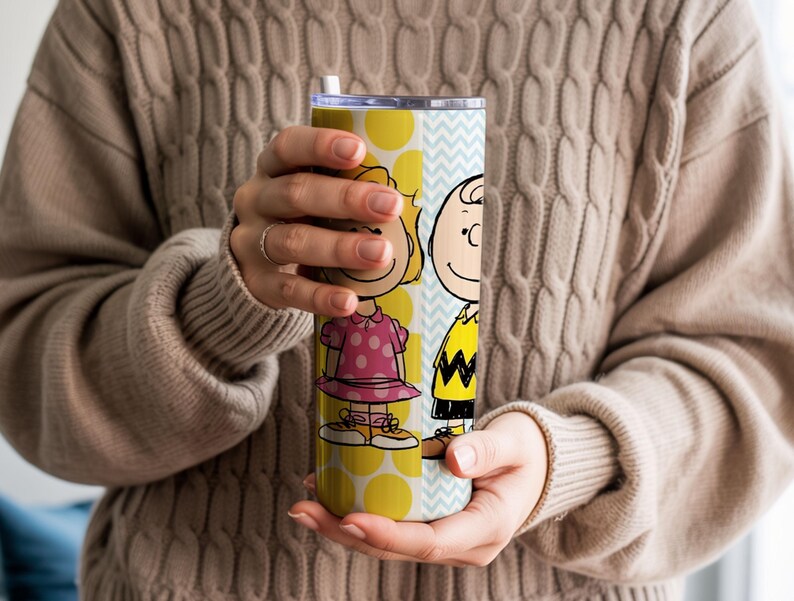 Puede incluir: Un vaso amarillo y azul claro con los personajes de dibujos animados Sally Brown y Charlie Brown. El vaso tiene una pajita blanca y un estampado de lunares amarillos. Los personajes visten sus trajes caracter&iacute;sticos.
