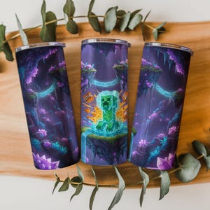 Puede incluir: Tres vasos aislados de acero inoxidable con un diseño de Minecraft. Los vasos presentan un paisaje de fantasía púrpura y azul con un personaje Creeper. El diseño incluye islas flotantes, cascadas y acentos brillantes.