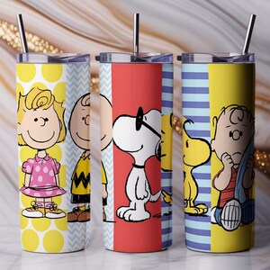 Puede incluir: Tres vasos de acero inoxidable con personajes de Peanuts. Cada vaso tiene un dise&ntilde;o diferente, incluyendo a Sally, Charlie Brown, Snoopy y Woodstock. Los vasos tienen un esquema de color amarillo, rojo y azul con una pajita negra.
