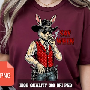 Peut inclure: T-shirt bordeaux avec un lapin cowboy portant des lunettes de soleil, un chapeau et un cigare. Le lapin porte un gilet rouge et tient une arme à feu. Le texte "SAY WHEN" est imprimé sur le t-shirt. Le texte "HIGH QUALITY 300 DPI PNG" est également présent.