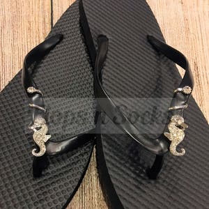 May include: Black flip flops with a rhinestone seahorse charm on each strap.