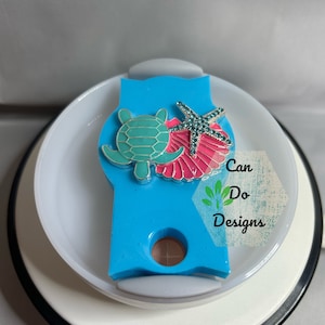May include: A blue and white lid with a sea turtle, starfish, and seashell design. The lid says "Can Do Designs".