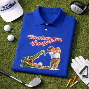 May include: Royal blue polo shirt with the phrase "I'm a huge fan of golf!" and a cartoon image of a golfer and alligator. Golf balls, a Titleist hat, golf club, and glove are also visible.