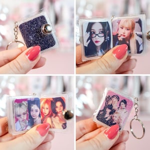 May include: Clear plastic keychain with a small, glittery, dark blue book-shaped charm. The keychain opens to reveal multiple photos of people. The keychain has a silver-colored metal ring.