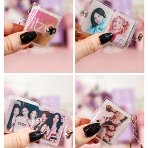 May include: Clear acrylic keychain with a silver keyring. The keychain features a small, openable book design. The book contains images of a musical group. The cover of the book has the word "ITZY" in pink and white.