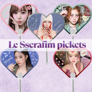 May include: Five heart-shaped hand fans featuring portraits of members of the group Le Sserafim, each with a unique border color and decorative stickers. The text Le Sserafim pickets is centered in purple font against a light purple background.