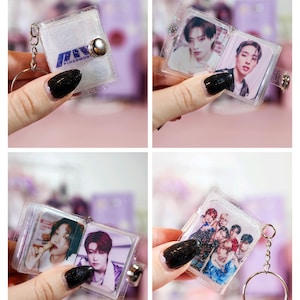 May include: Clear, glittery mini photo album keychain. The album features images of a musical group. The album is attached to a silver keyring. The album has the word "PIHARMONY" printed on the cover.
