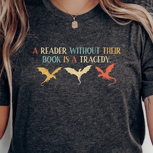 Op de afbeelding: Donkergrijs V-hals T-shirt met de quote "A reader without their book is a tragedy." Het shirt heeft drie drakenillustraties in geel, wit en rood. Het shirt is gemaakt van een zacht materiaal.