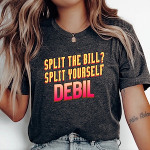 Peut inclure: Un t-shirt à manches courtes gris anthracite chiné portant l'inscription "SPLIT THE BILL? SPLIT YOURSELF DEBIL" imprimée en lettres grasses avec un dégradé de jaune à rose et un effet d'ombre portée au centre de la poitrine.