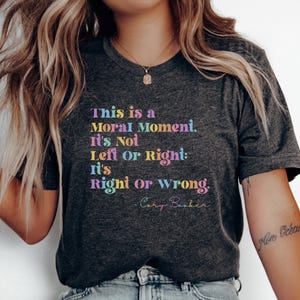 Op de afbeelding: Donkergrijs t-shirt met de quote "This is a Moral Moment. It's Not Left or Right: It's Right or Wrong. - Cory Booker" in regenboogkleuren. Het shirt heeft een V-hals.