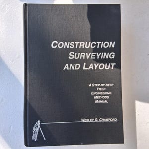 May include: A black hardback book titled Construction Surveying and Layout, A Step-by-Step Field Engineering Methods Manual by Wesley G. Crawford. The cover features white text and a small white line drawing of a surveyor using a tripod instrument.
