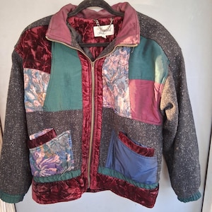 May include: A zip-up jacket featuring a patchwork design of dark gray speckled wool-like fabric, deep red velvet panels, and floral patterned sections. The garment includes a high collar, two front pockets, and a label reading The Legend.