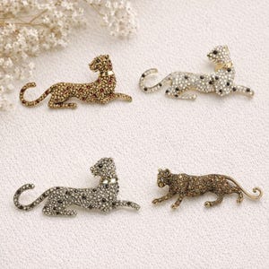 Può includere: Quattro spille a forma di leopardo impreziosite da gioielli in vari colori. Le spille sono sdraiate, con la testa sollevata. Le spille sono dorate, argentate e bronzate, con accenti di cristallo nero, rosso e trasparente. Le spille hanno un colletto dorato.