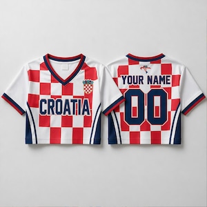 Op de afbeelding: Een gecropt Kroati&euml; voetbalshirt met een rood-wit geblokt patroon en een V-hals. De voorkant toont "CROATIA" en een wapen. De achterkant heeft "YOUR NAME" boven het nummer "00". Marineblauwe accenten en afwerking.