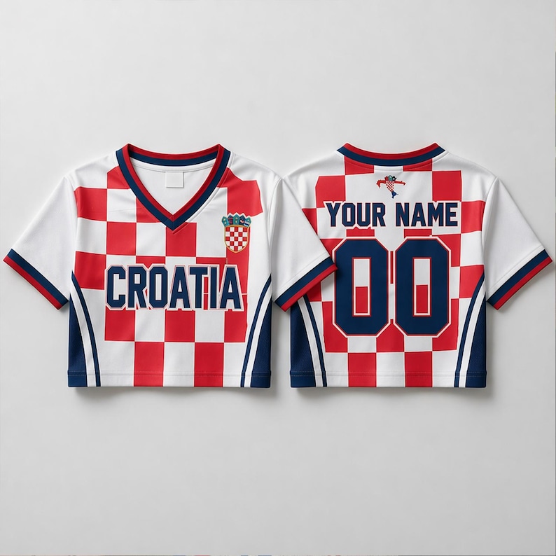 Op de afbeelding: Een gecropt Kroati&euml; voetbalshirt met een rood-wit geblokt patroon en een V-hals. De voorkant toont "CROATIA" en een wapen. De achterkant heeft "YOUR NAME" boven het nummer "00". Marineblauwe accenten en afwerking.