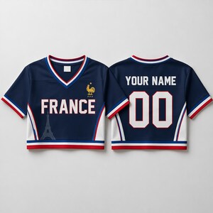 May include: Navy blue crop top jersey with white and red trim. The front displays "FRANCE" and an Eiffel Tower graphic. The back has "YOUR NAME" and the number "00". A golden rooster emblem is on the front.