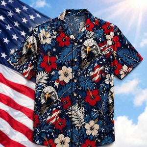 Puede incluir: Camisa de manga corta con fondo azul marino. La camisa presenta un estampado repetido de banderas americanas, águilas calvas, flores de hibisco rojas, flores blancas y hojas azules. La camisa tiene un cuello clásico y botones de madera.