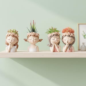 May include: Four decorative girl-shaped planters with closed eyes and floral headbands. Each planter holds a different succulent or flower. The planters are in shades of beige, pink, and white, and are arranged on a light-colored shelf against a green wall.