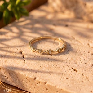 Può includere: Un anello in oro caratterizzato da una serie di incastonature a forma di marquise, ciascuna contenente una piccola pietra chiara. La fascia presenta un dettaglio testurizzato a perline lungo la circonferenza, creando un motivo ripetitivo.