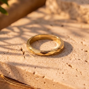 May include: A gold-toned metal ring featuring a faceted, geometric band design. The ring has a polished, reflective surface with multiple angled planes around the exterior circumference, creating a series of small, repeating triangular shapes.