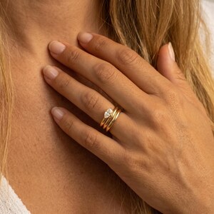 May include: A set of three gold rings. The top ring features a pear-shaped diamond. The other two rings are simple gold bands. The rings are stacked on a finger.