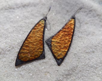 May include: A pair of gold and black earrings with a textured surface. The earrings are shaped like triangles with rounded edges.