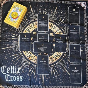 May include: A black and gold Celtic Cross tarot spread cloth with a matching tarot deck. The cloth features a central design with symbols and the words "Celtic Cross". Ten tarot cards are laid out on the cloth.