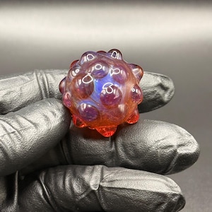May include: A spherical glass object with a textured surface featuring multiple raised bumps. The glass displays a gradient of colors, transitioning from deep purple and blue tones in the center to a vibrant, translucent orange at the base.