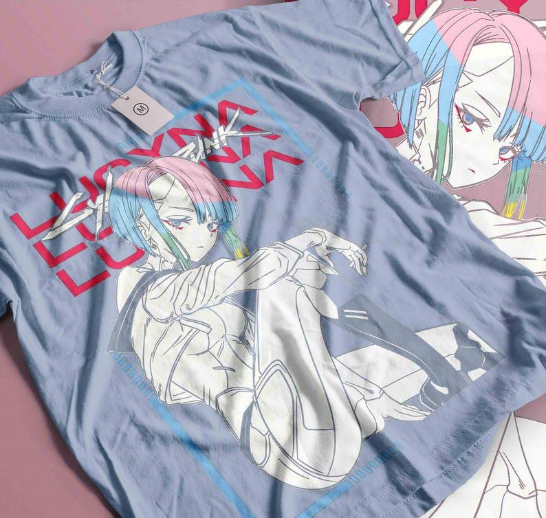 May include: A pale blue t-shirt with an anime-style character graphic with pink and blue hair. The shirt features the text "LUCKY" in red and "V" in a blue box. A tag is attached to the shirt.