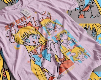 May include: A light pink t-shirt featuring a cartoon illustration of a character with long blonde hair, blue eyes, and a sailor uniform. The shirt has Japanese text and the name "MINAKO AINO" printed on it. The design includes multiple panels with different poses of the character.