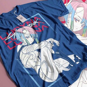 May include: A navy blue t-shirt with a graphic of an anime character with blue, pink, and green hair. The text "Cyberpunk" is in red and white. The design is framed in a light blue rectangle.