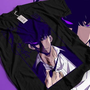 May include: Black t-shirt featuring a purple anime-style illustration of a character with dark hair and purple accents. The design includes text and a tag. The shirt is displayed on a purple surface.