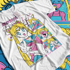 May include: White t-shirt featuring a colorful anime-style illustration. The design includes a central character with blonde hair, blue eyes, and a pink and blue outfit, along with Japanese text and the name "USAGI TSUKINO".