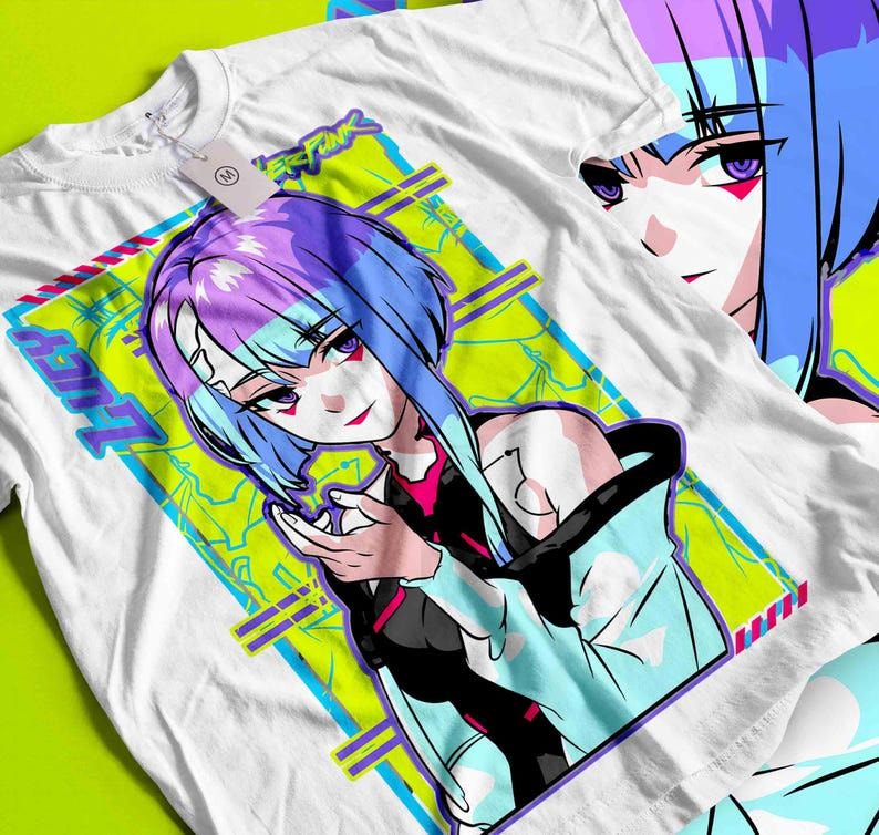 May include: White t-shirt featuring a colorful anime-style illustration of a female character with blue and purple hair. The design includes the word "LUCY" and other text within a geometric frame. A second shirt with a partial image is visible.