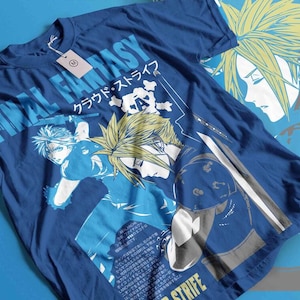 May include: Blue t-shirt featuring a graphic of a character from Final Fantasy. The design includes the text "FINAL FANTASY" and Japanese characters. The character has spiky blonde hair and is holding a sword. A tag is attached to the shirt.