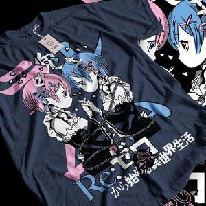 May include: Navy blue t-shirt with an anime graphic of two characters with pink and blue hair, linked by a chain. The shirt includes Japanese text and a pink arrow design. A white tag is attached.