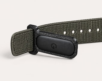 May include: An olive green woven nylon watch strap featuring a black textured plastic connector piece. The connector has a small, embossed letter G logo on its surface. The strap includes a series of evenly spaced adjustment holes for sizing.