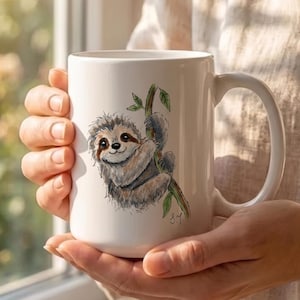 May include: A white ceramic mug featuring a watercolour-style illustration of a brown and grey sloth hanging from a green leafy branch. The sloth has a smiling expression, and the initials S.J. are visible in black ink near the bottom of the branch.