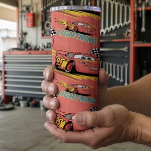 May include: A red tumbler featuring the character Lightning McQueen from the movie Cars. The tumbler has a repeating pattern of the character with the text "Lightning" and the number "95". The background is a yellow and black design.