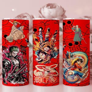 May include: Three red tumblers with anime-style illustrations. Each tumbler features a different character from the One Piece series. The tumblers have a red background with a repeating skull and crossbones design.