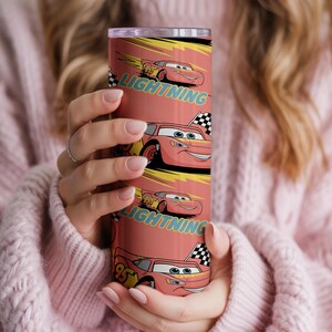 May include: A red tumbler featuring the character Lightning McQueen from the movie Cars. The tumbler has a repeating pattern of the character and the word "Lightning". The design includes a checkered flag and the number 95.