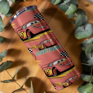 May include: A red tumbler featuring a repeating pattern of the character Lightning McQueen from the movie Cars. The design includes the number 95, checkered flags, and the word "Lightning". The tumbler has a silver lid.